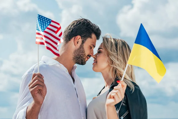Mujer atractiva y hombre guapo sosteniendo banderas americanas y ucranianas - foto de stock