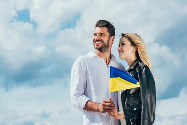 Attractive woman and handsome man holding ukrainian flag outside — Stock Photo