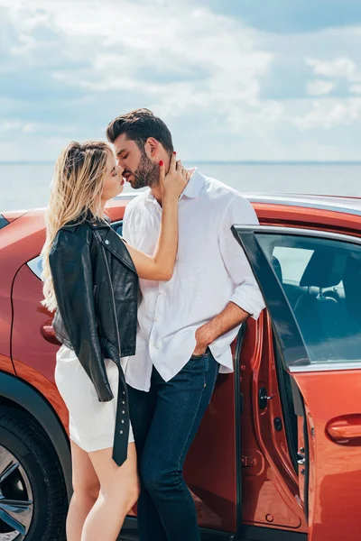 Atractiva mujer y hombre guapo besándose y abrazándose cerca del coche - foto de stock