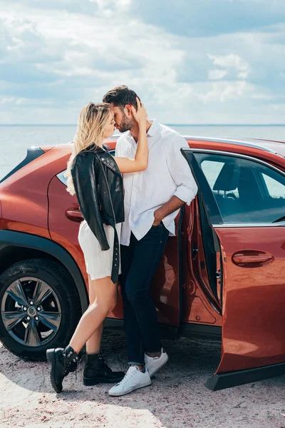 Привлекательная женщина и красивый мужчина целуются и обнимаются возле машины — стоковое фото