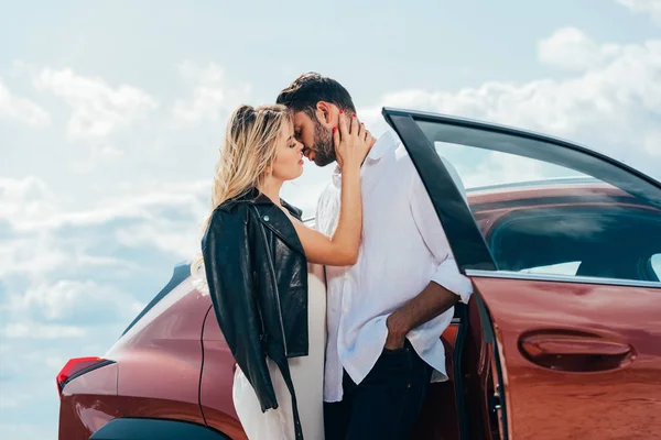 Atractiva mujer y hombre guapo besándose y abrazándose cerca del coche - foto de stock