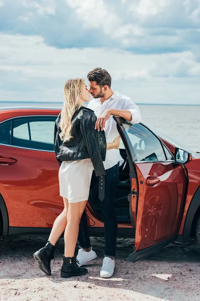Привлекательная женщина и красивый мужчина целуются и обнимаются возле машины — стоковое фото