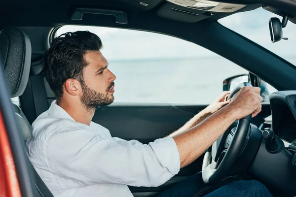 Hombre guapo en camisa blanca conduciendo coche y mirando hacia otro lado - foto de stock