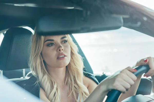 Mujer atractiva y rubia sentada en coche y mirando hacia otro lado - foto de stock