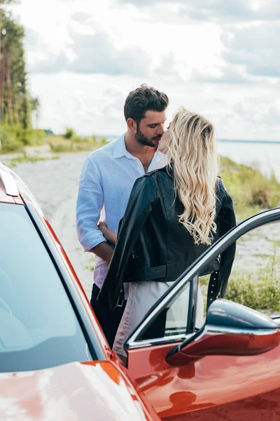 Femme blonde et bel homme embrasser et étreindre près de la voiture — Photo de stock