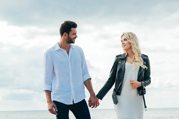 Atractiva mujer y hombre guapo sonriendo y tomados de la mano - foto de stock