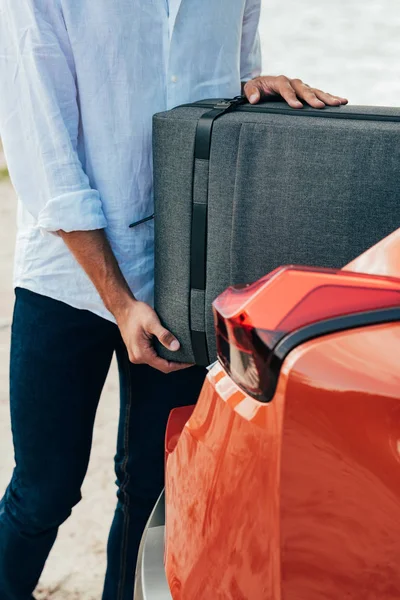 Cropped view of man in shirt putting suitcase in car — Stock Photo