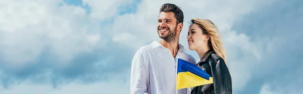 Tiro panorâmico de mulher atraente e homem bonito sorrindo e segurando bandeira ucraniana — Fotografia de Stock