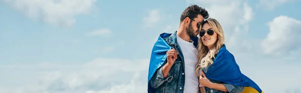 Panoramic shot of attractive woman and handsome man smiling and holding ukrainian flag — Stock Photo