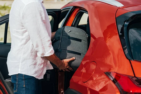 Ausgeschnittener Blick auf Mann im Hemd, der Rucksack ins Auto legt — Stockfoto