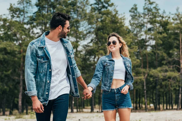 Donna attraente e bell'uomo in giubbotti di jeans sorridente e tenendosi per mano — Foto stock