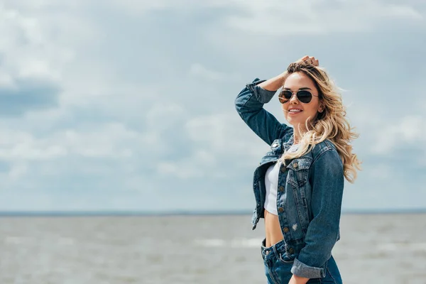 Blonde and attractive woman in denim jacket and sunglasses looking away — Stock Photo