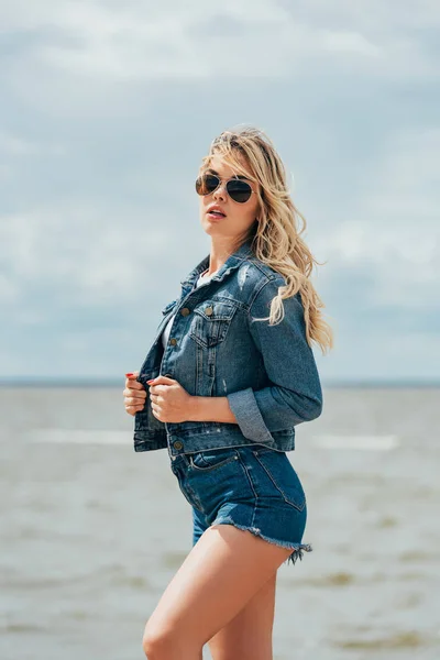 Blonde und attraktive Frau in Jeansjacke und Sonnenbrille schaut weg — Stockfoto