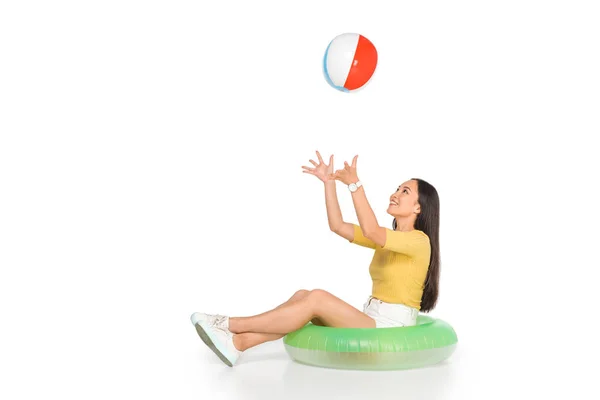 Young asian woman sitting on swim ring and playing beach ball on white background — Stock Photo