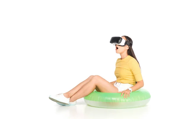 Удивлена азиатская женщина с помощью гарнитуры виртуальной реальности, сидя на плавательном кольце на белом фоне — стоковое фото
