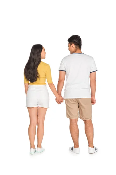 Vista posterior de hombre y mujer jóvenes en ropa de verano cogidos de la mano sobre fondo blanco - foto de stock