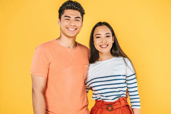 Cheerful asian couple embracing while smiling at camera isolated on yellow — Stock Photo