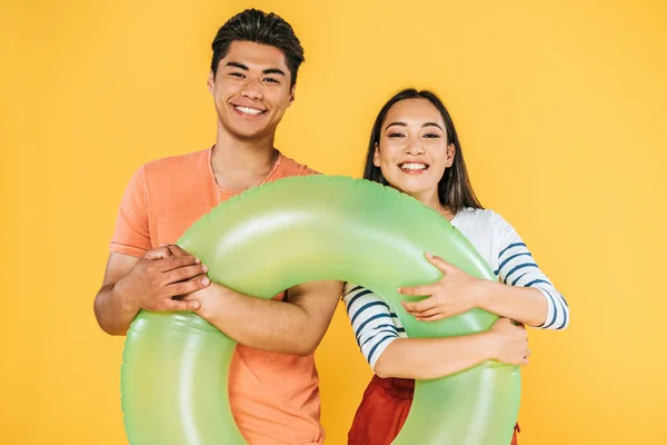 Happy asian man and woman holding swim ring and smiling at camera isolated on yellow — Stock Photo