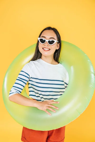 Belle asiatique fille en lunettes de soleil regardant loin tout en tenant anneau de nage isolé sur jaune — Photo de stock