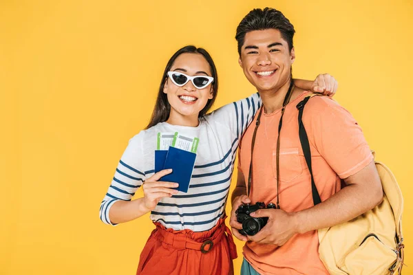 Happy asian girl holding passports and air tickets while hugging smiling boyfriend isolated on yellow — Stock Photo