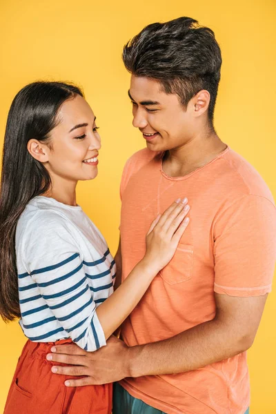 Happy asian man and woman hugging while looking at each other isolated on yellow — Stock Photo