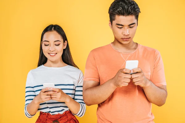 Junge asiatische Mann und Frau mit Smartphones isoliert auf gelb — Stockfoto