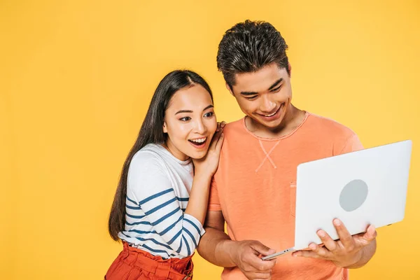 Junge asiatische Mann mit Laptop in der Nähe aufgeregt Freundin isoliert auf gelb — Stockfoto