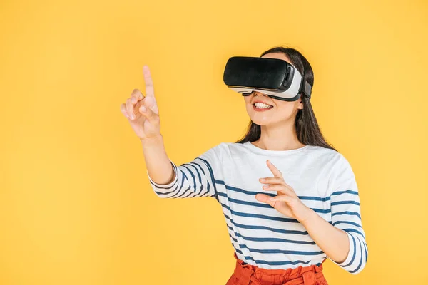 Niña sonriente haciendo gestos mientras usa auriculares de realidad virtual aislados en amarillo - foto de stock