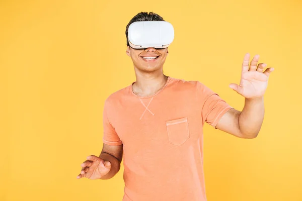 Uomo sorridente gesticolando durante l'utilizzo di cuffie realtà virtuale isolato su giallo — Foto stock