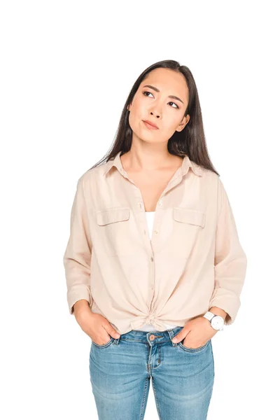 Thoughtful asian woman holding hands in pockets while looking away isolated on white — Stock Photo