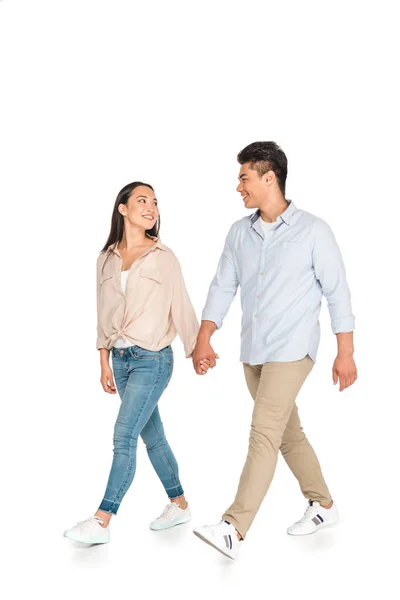 Feliz asiática pareja cogida de la mano y mirando el uno al otro mientras caminando sobre blanco fondo - foto de stock