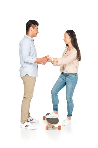 Handsome asian man helping girlfriend standing on longboard on white background — Stock Photo