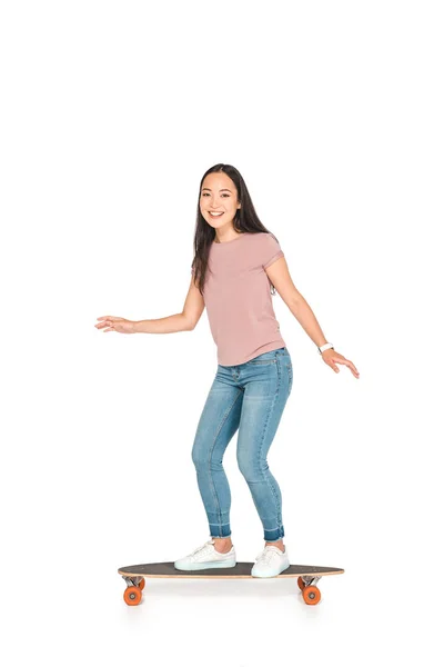 Весёлая азиатская девушка едет на длинной доске и улыбается в камеру на белом фоне — стоковое фото