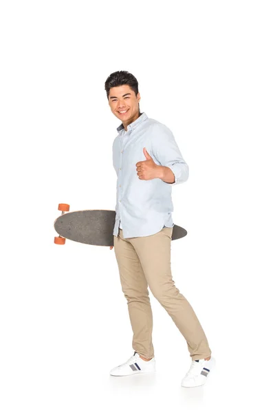 Giovane asiatico uomo holding longboard mentre mostra pollice su su bianco sfondo — Foto stock