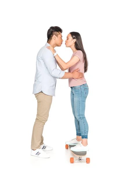 Young asian man hugging and kissing girlfriend standing on longboard on white background — Stock Photo