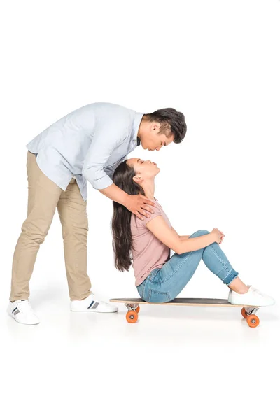 Красивий азіатський чоловік обіймає і цілує дівчину, сидячи на дошці на білому тлі — стокове фото