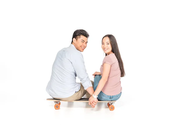 Joyeux asiatique couple assis sur longboard et souriant à caméra sur fond blanc — Photo de stock