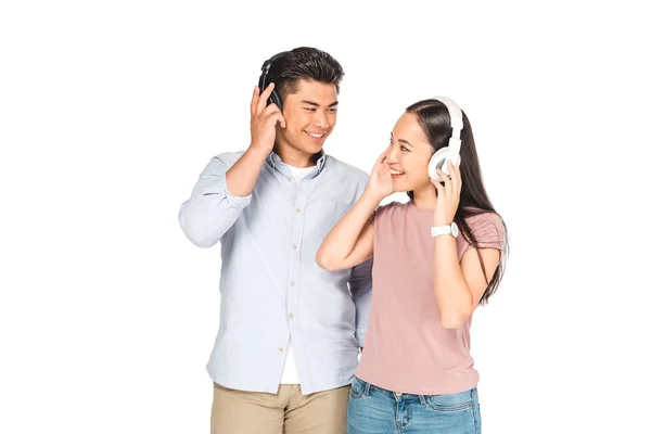 Cheerful asian couple looking at each other while listening music in headphones isolated on white — Stock Photo