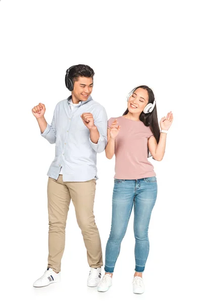 Feliz pareja asiática mirándose mientras escucha música en auriculares y bailando sobre fondo blanco - foto de stock