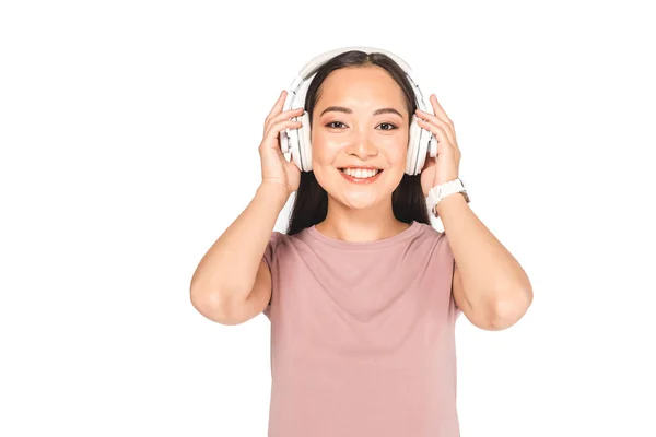 Atractivo asiático chica sonriendo a cámara mientras escucha música en auriculares aislado en blanco - foto de stock