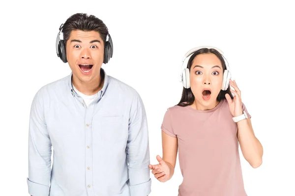 Chocado ásia homem e mulher olhando para câmera enquanto ouvindo música em fones de ouvido isolado no branco — Fotografia de Stock