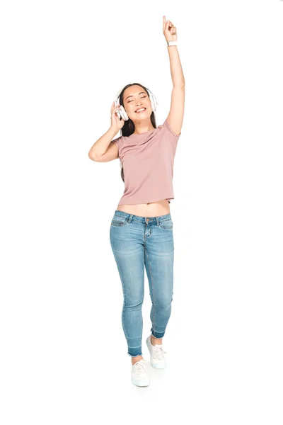 Cheerful asian girl listening music in headphones and dancing with closed eyes on white background — Stock Photo