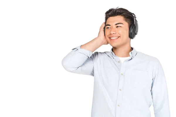 Fröhlicher asiatischer Mann, der mit Kopfhörern Musik hört, lächelt und isoliert auf weißem Grund wegschaut — Stockfoto