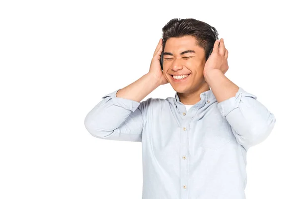 Excitado asiático hombre escuchando música en auriculares con los ojos cerrados aislado en blanco - foto de stock