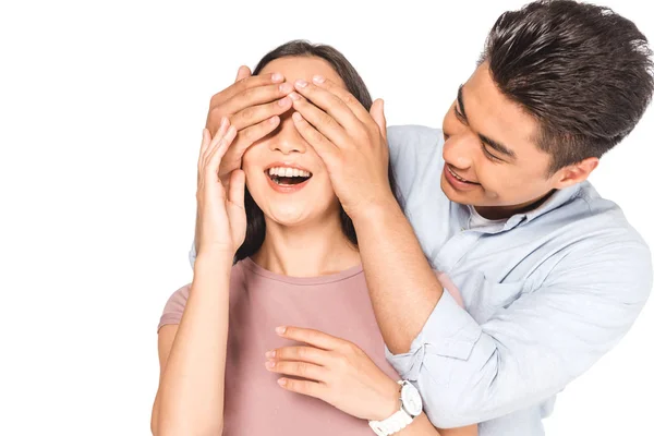 Handsome asian man closing eyes of cheerful girlfriend with hands isolated on white — Stock Photo