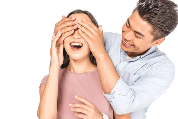 Усміхнений азіатський чоловік закриває очі веселої дівчини з руками ізольовані на білому — стокове фото