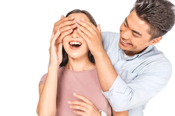 Sonriente asiático hombre cerrando ojos de alegre novia con manos aisladas en blanco - foto de stock