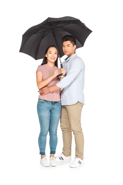 Joven asiático hombre abrazando novia mientras de pie bajo paraguas juntos en blanco fondo - foto de stock