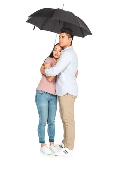 Guapo asiático hombre abrazando bonito novia mientras de pie bajo paraguas en blanco fondo - foto de stock