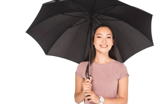 Hübsche asiatische Mädchen hält schwarzen Regenschirm und lächelt in die Kamera isoliert auf weiß — Stockfoto